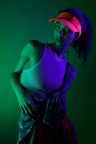 stock image A young woman poses against a green backdrop, bathed in neon lights. Her sporty attire and confident gaze create a vibrant image.