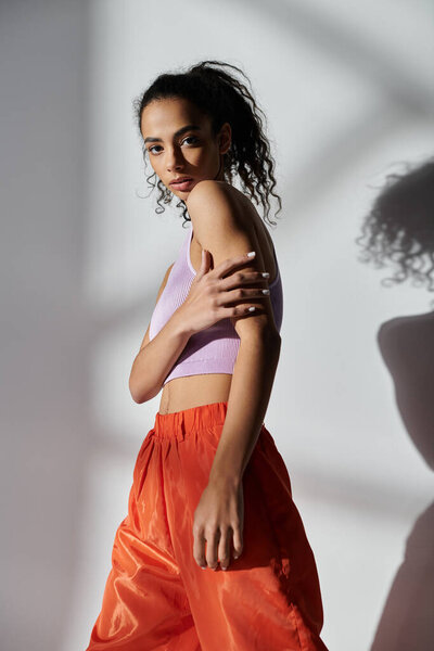 Стильная афроамериканка позирует в студии на сером фоне, демонстрируя свой модный наряд.