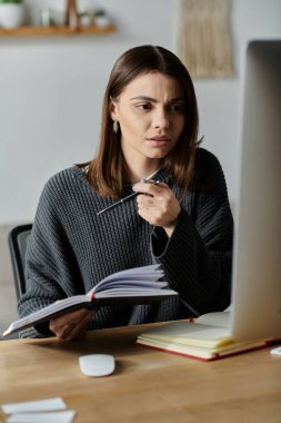 A young woman in a grey sweater thoughtfully works on content creation at her home office desk. clipart