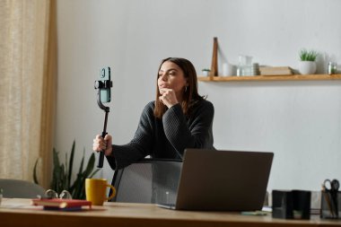 Gri kazaklı genç bir kadın ev ofisinde oturup dijital pazarlama işi için içeriği filme alıyor..