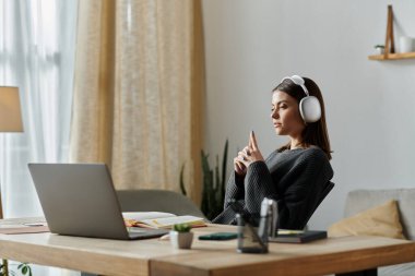 Gri kazaklı genç bir kadın ev bilgisayarında çalışıyor, kulaklıkları açık müzik dinliyor..