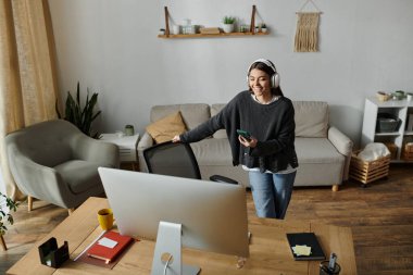 Gri kazaklı genç bir kadın ofis masasında çalışırken gülümsüyor..