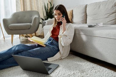 Genç bir kadın sıradan bir kıyafetle yerde oturuyor, laptopuyla çalışıyor ve telefonuyla konuşuyor..