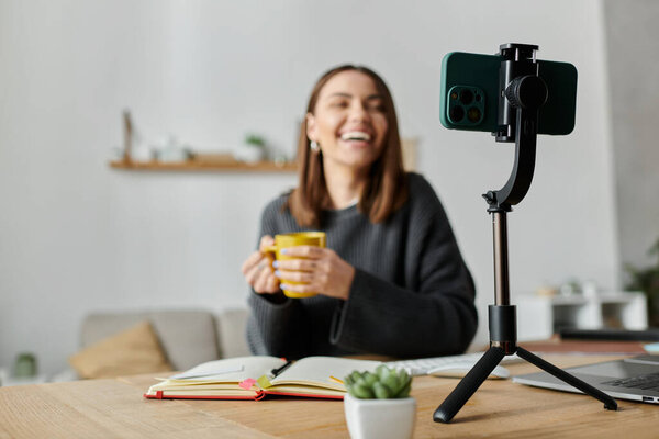 Молодая женщина ярко улыбается, когда отдыхает от работы, держа в руке кружку кофе..