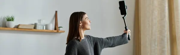 Stock image A young woman films content for her online audience while working remotely from her home.