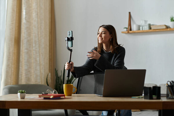 Молодая женщина в сером свитере сидит за своим столом, снимая контент для своей онлайн-аудитории.