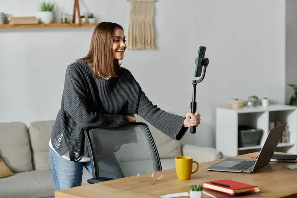 stock image A young woman in a grey sweater films a video while sitting at a table in her home office.