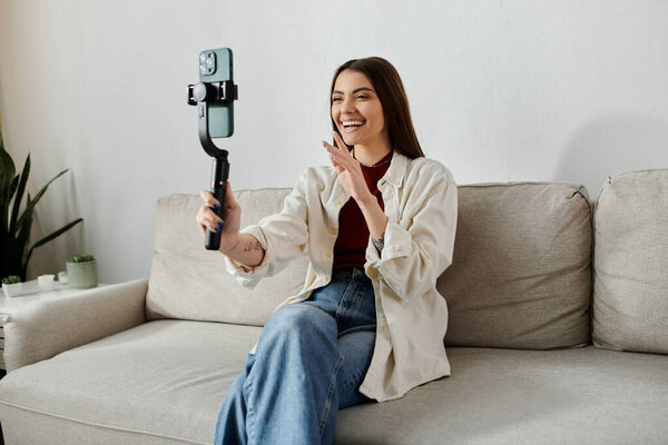 Молодая женщина в повседневной одежде улыбается и снимает видеоблог, сидя на диване.