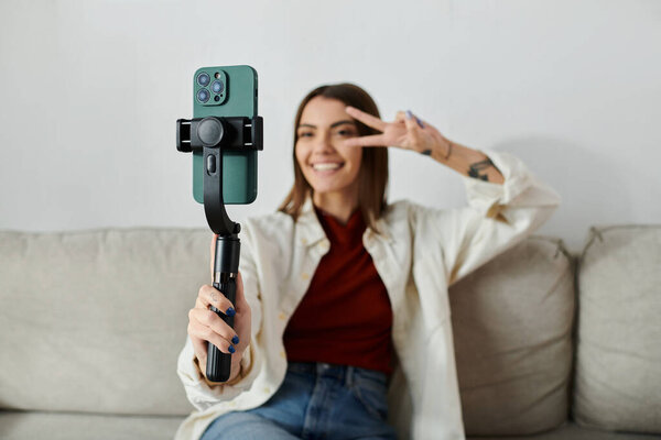 Молодая женщина случайно одетые фильмы содержание для своего видеоблога с помощью стабилизатора смартфона, сидя на диване.