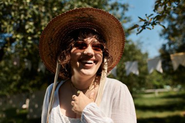 Hasır şapkalı genç bir kadın yaz bahçesinde güneşli bir günün tadını çıkarırken ışıl ışıl gülümsüyor..