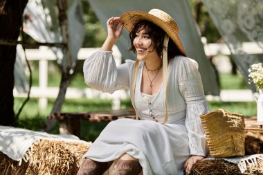 A young woman in a white dress and straw hat smiles brightly while sitting in a summer garden, enjoying the sunshine. clipart