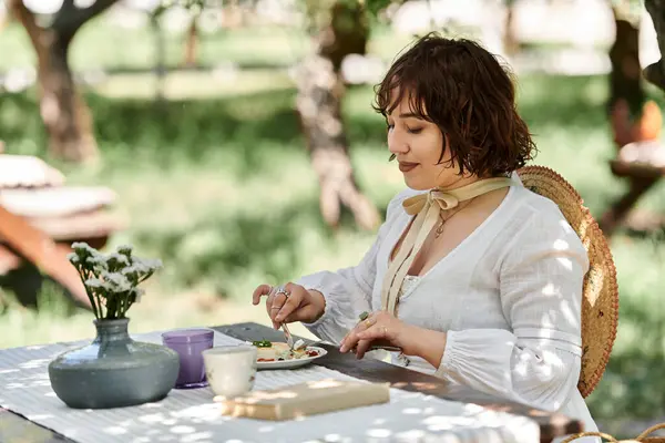 stock image A young woman enjoys a summer brunch outdoors, dressed in a white dress and a straw hat.