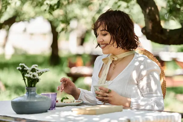 stock image A young woman in a white dress enjoys a leisurely brunch in a lush garden setting.