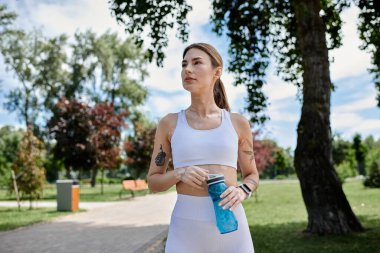 Vitiligo 'su olan genç bir sporcu parktaki antrenmanına ara veriyor. İleriye bakarken elinde bir su şişesi tutuyor..