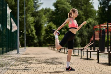 Vitiligo 'su olan genç bir kadın, parkta pembe bir bluz ve siyah şort giyerken bacağını esnetiyor..