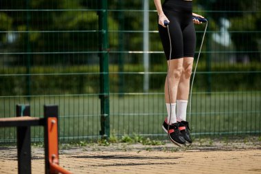 A young woman in black shorts jumps rope outdoors. She is wearing white socks and black sneakers with red accents. clipart