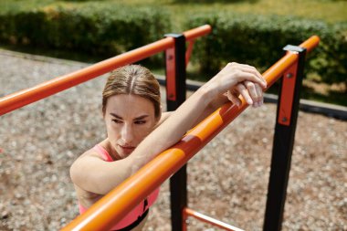 Vitiligo 'lu genç bir sporcu, pembe bir bluz giyiyor, açık hava antrenmanı sırasında parkta bir bara yaslanıyor..