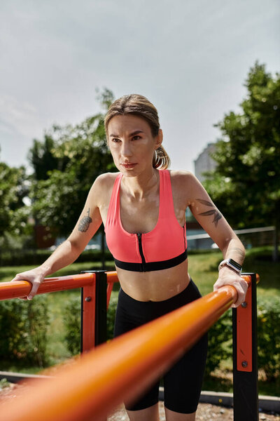 Молодая женщина с витилиго, одетая в розовый топ, работает на параллельных барах в солнечном парке.