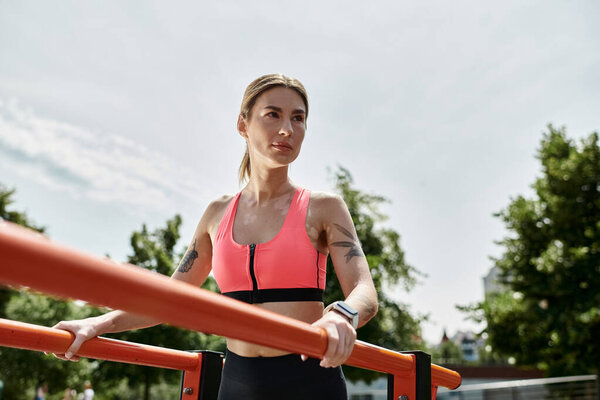 Молодая женщина с витилиго работает на параллельных барах в парке, в розовом спортивном бюстгальтере и черных леггинсах.