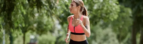 Stock image A young woman with vitiligo runs through a park, wearing a pink sports bra and black leggings.