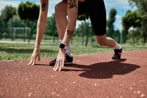 Молодая женщина с витилиго и татуировкой в активной одежде готовится бежать по треку, ее рука тянется к земле.