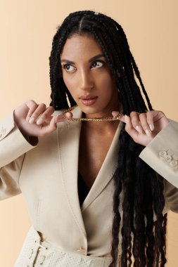 A young woman with braided black hair poses in a beige blazer with a gold chain necklace. clipart