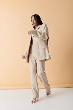 A young African American woman in a beige suit walks confidently towards the camera. clipart