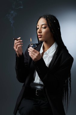 A stylish woman in a white shirt and black blazer lights a cigarette with a lighter. clipart