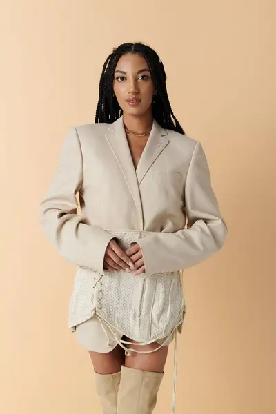 stock image A young woman in a cream blazer, skirt and boots poses against a beige backdrop.