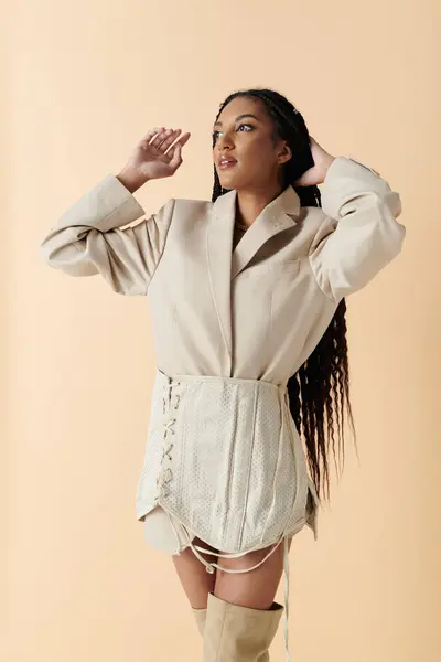 stock image A stylish young woman poses in a cream blazer and corset, her long black braids falling down her back.