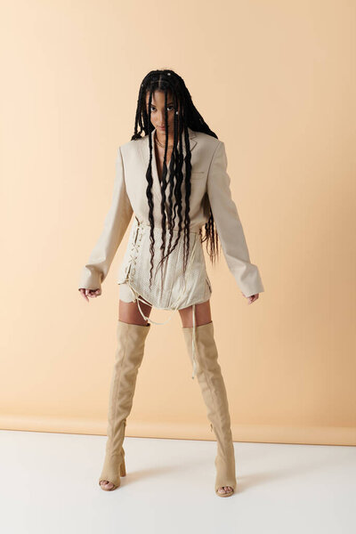 Стильная афроамериканка в 20 лет уверенно позирует в модном наряде на бежевом фоне..