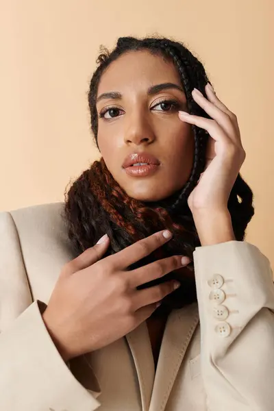 stock image A young woman with braids and a warm smile poses in a beige blazer against a beige background.