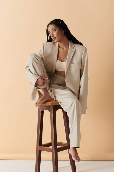 Молодая женщина в стильном бежевом костюме сидит на стуле и смотрит в сторону от камеры..
