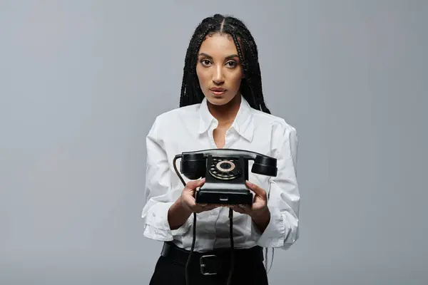 stock image A young woman in a white shirt holds an old rotary phone, posing against a gray backdrop.