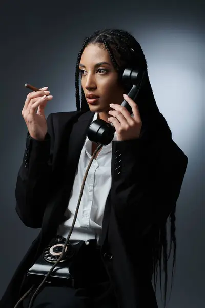 stock image A stylish woman in a white shirt and black blazer poses with a vintage phone against a grey backdrop.