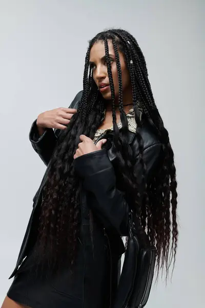 stock image In a studio, a young African American woman poses in a black leather jacket and animal print top, long black braids cascading down her back