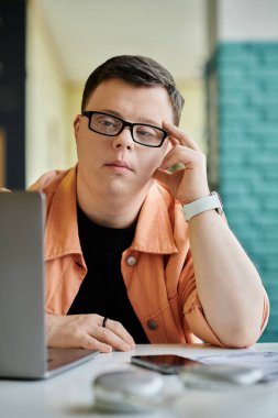 Down sendromlu genç bir adam bir kafede dizüstü bilgisayarıyla çalışıyor ve görevine odaklanıyor..