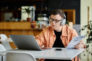Down sendromlu bir adam bir kafede dizüstü bilgisayarıyla çalışıyor, kulaklıkları açık, işine odaklanmış..