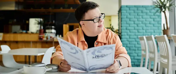 stock image A man with Down syndrome sits at a cafe table, thoughtfully reading a menu, considering his meal options.