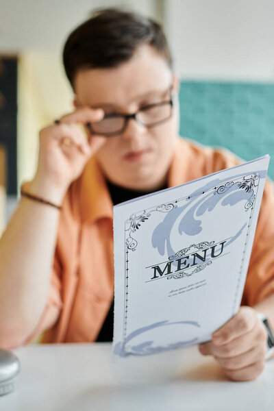 Человек с синдромом Дауна внимательно рассматривает меню в кафе, выбирая, что заказать..