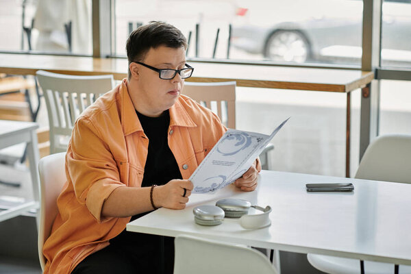 Человек с синдромом Дауна сидит за столиком кафе, внимательно рассматривая меню.