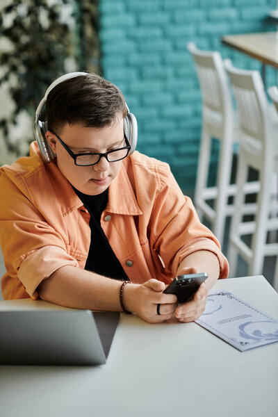 A man with Down Syndrome works on his laptop and phone while enjoying a cafe.