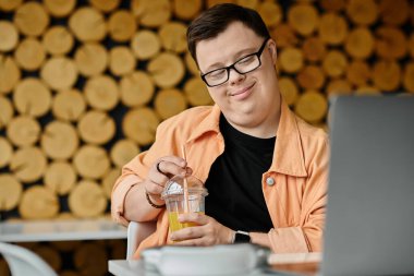 A man with Down syndrome smiles as he works on his laptop in a cafe, enjoying a refreshing drink during his workday. clipart