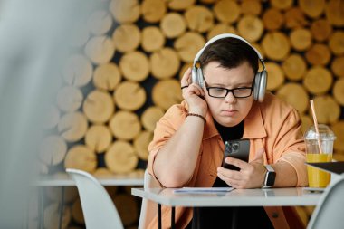 A man with Down syndrome works on his laptop in a cafe, headphones on, focused on his work. clipart