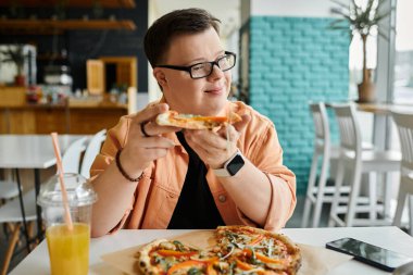 Down sendromlu bir adam bir kafede bir dilim pizzanın tadını çıkarıyor, yemeğin tadını çıkarıyor ve arkadaşlığın tadını çıkarıyor..