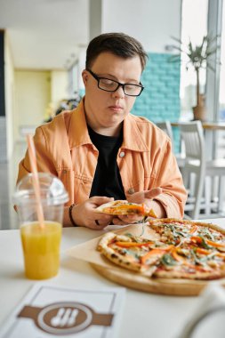Down sendromlu bir adam kafe ortamında bir dilim pizzanın tadına bakar..