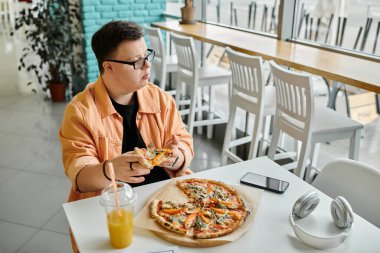 Down sendromlu bir adam bir kafede bir masada oturuyor ve bir dilim pizzanın tadını çıkartıyor..