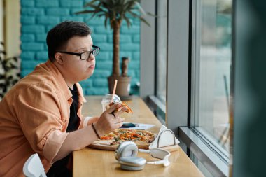 Down sendromlu bir adam kafenin tadını çıkarırken bir dilim pizzanın tadını çıkarır..