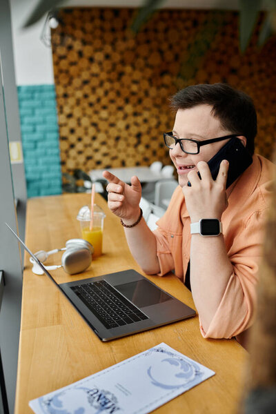 A man with Down syndrome works remotely on his laptop at a cafe, talking on his phone.