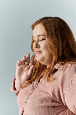 A plus size woman in a pink shirt, with her eyes closed, raises her hand as if in prayer. clipart